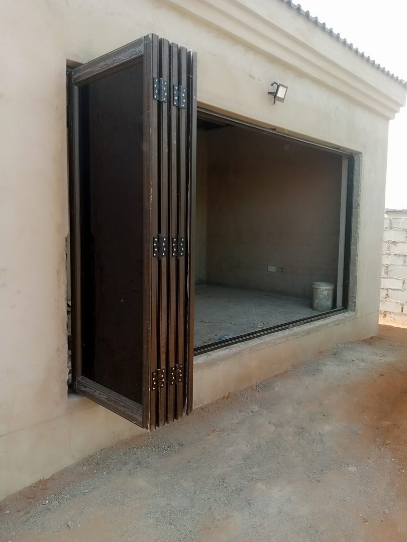 Five-panel aluminium bifold door folded and stacked fully open, wood-grain bronze frames, new house in Gaborone North — Tshipiworks