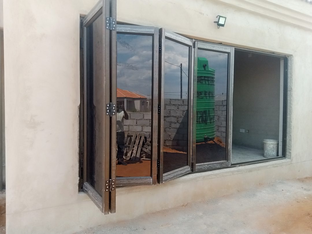 Partly folded five-panel aluminium folding door with tinted glass on a new house in Gaborone North — Tshipiworks