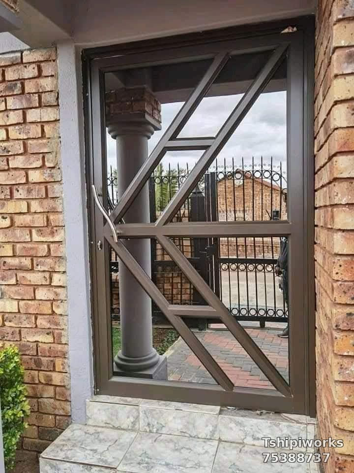 Bronze geometric V-pattern aluminium door with glazed panels at a brick home — Tshipiworks