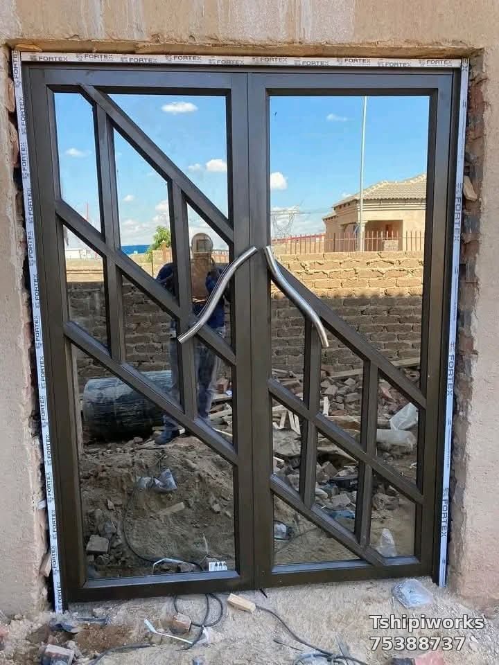 Pair of dark geometric aluminium double entrance doors with curved handles on site — Tshipiworks