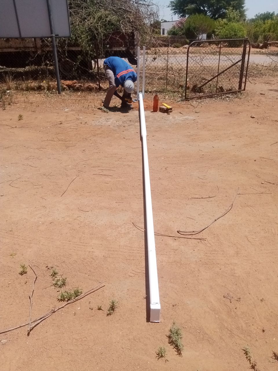 Tshipiworks fitter joining a white steel flag pole to its base sleeve on site in Tlokweng