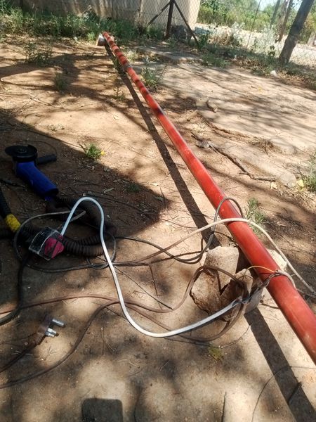 Red-painted steel flag pole being prepared in the Tshipiworks workshop with an angle grinder