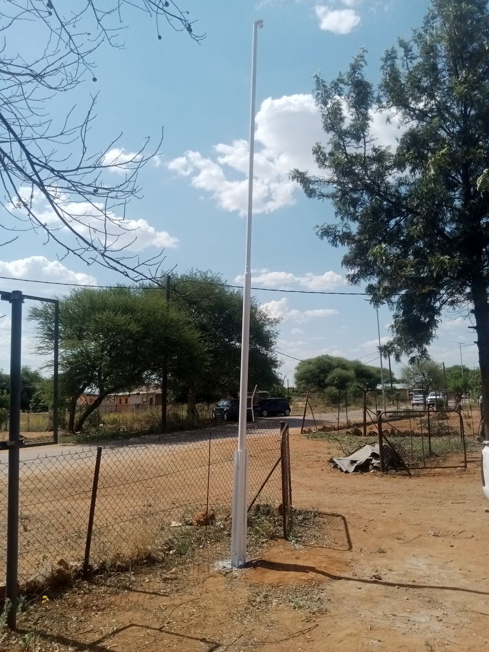 White steel flag pole made and installed by Tshipiworks in Tlokweng, Botswana, standing in a square base sleeve set in concrete