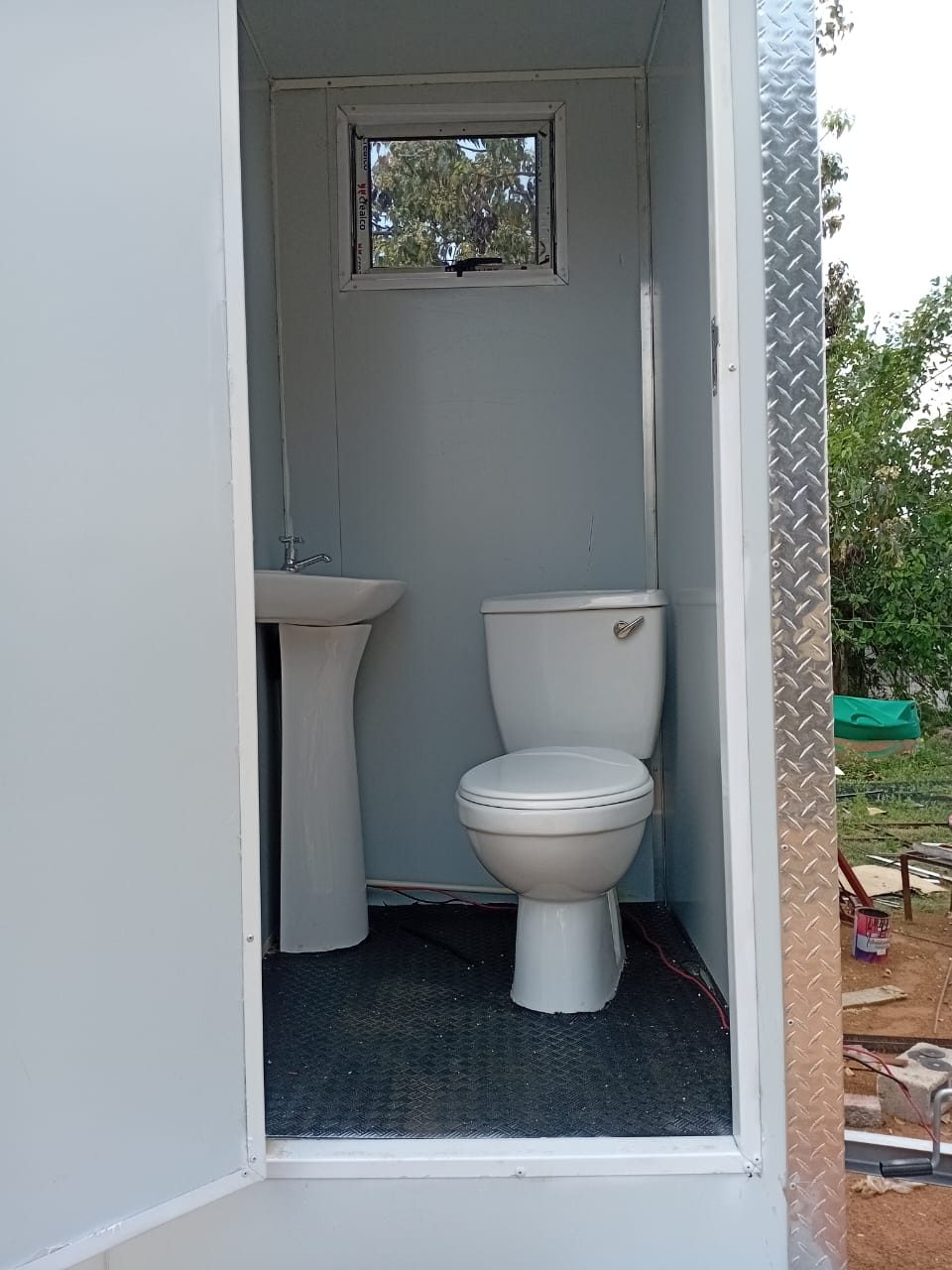 Inside one cubicle: flush toilet, pedestal basin, small aluminium window and rubber floor matting