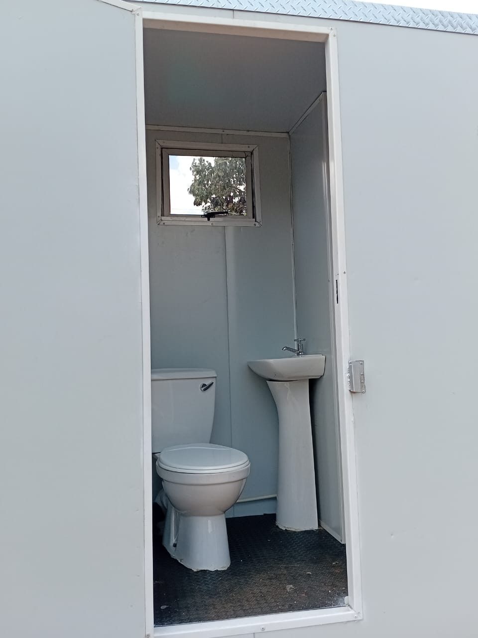 Second cubicle interior with flush toilet, pedestal basin and tap, and aluminium window