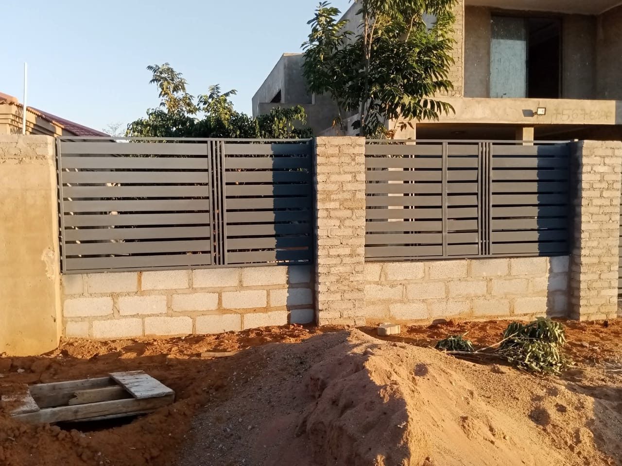 Grey horizontal steel slat fence panels on concrete block wall — Tshipiworks