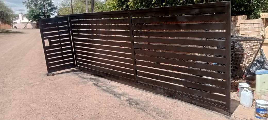 Black horizontal slat sliding gate partially open on residential driveway — Tshipiworks