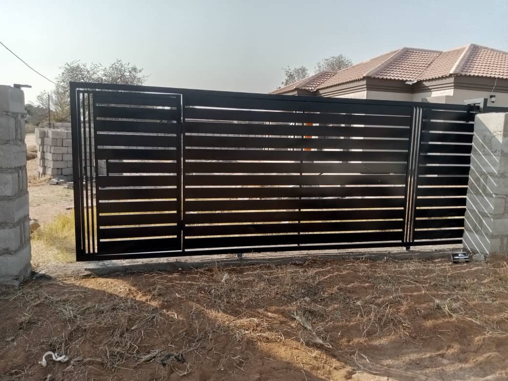 Low-angle view of black horizontal slat sliding gate and track — Tshipiworks