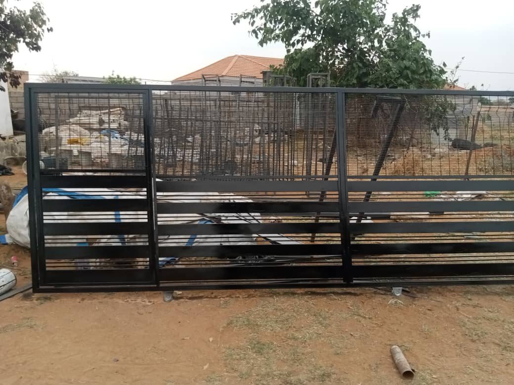Black mesh sliding gate partially open on construction site — Tshipiworks