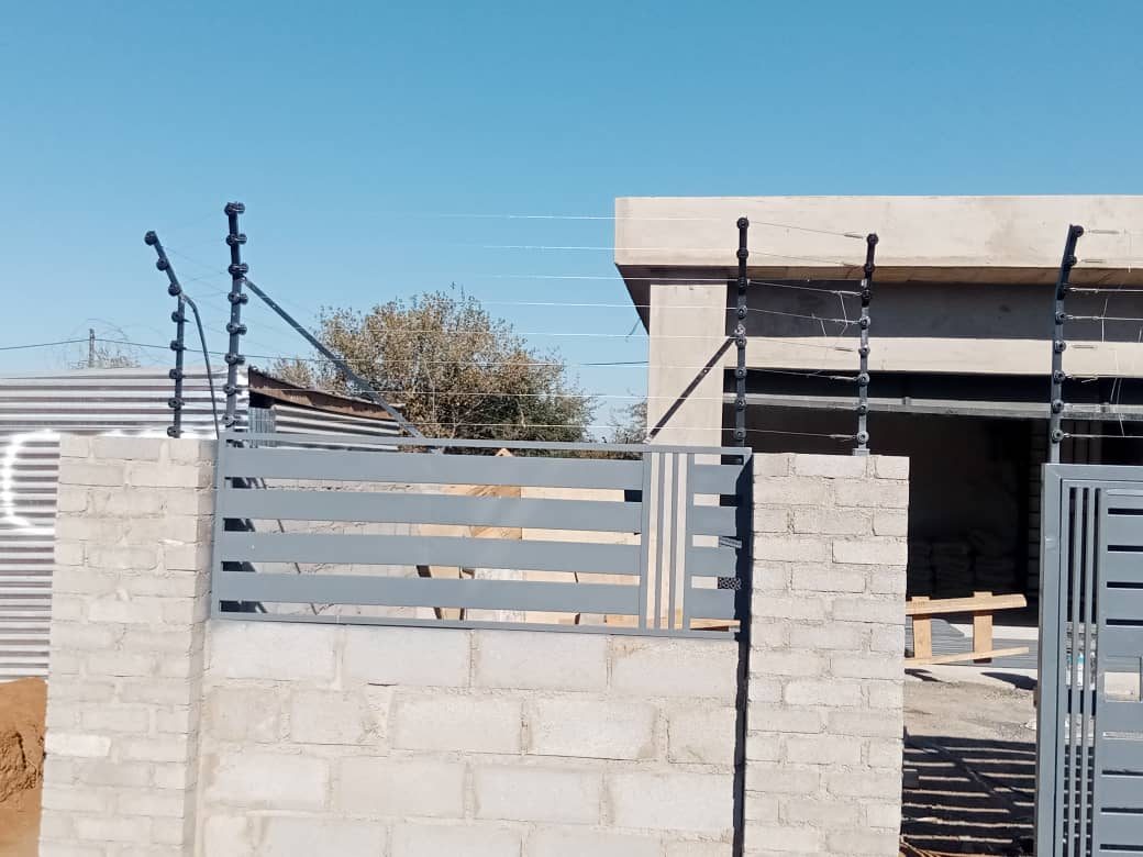 Grey horizontal slat fencing with electric fence wires on top — Tshipiworks
